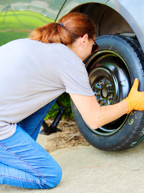 A woman mounts a spare tire on a car